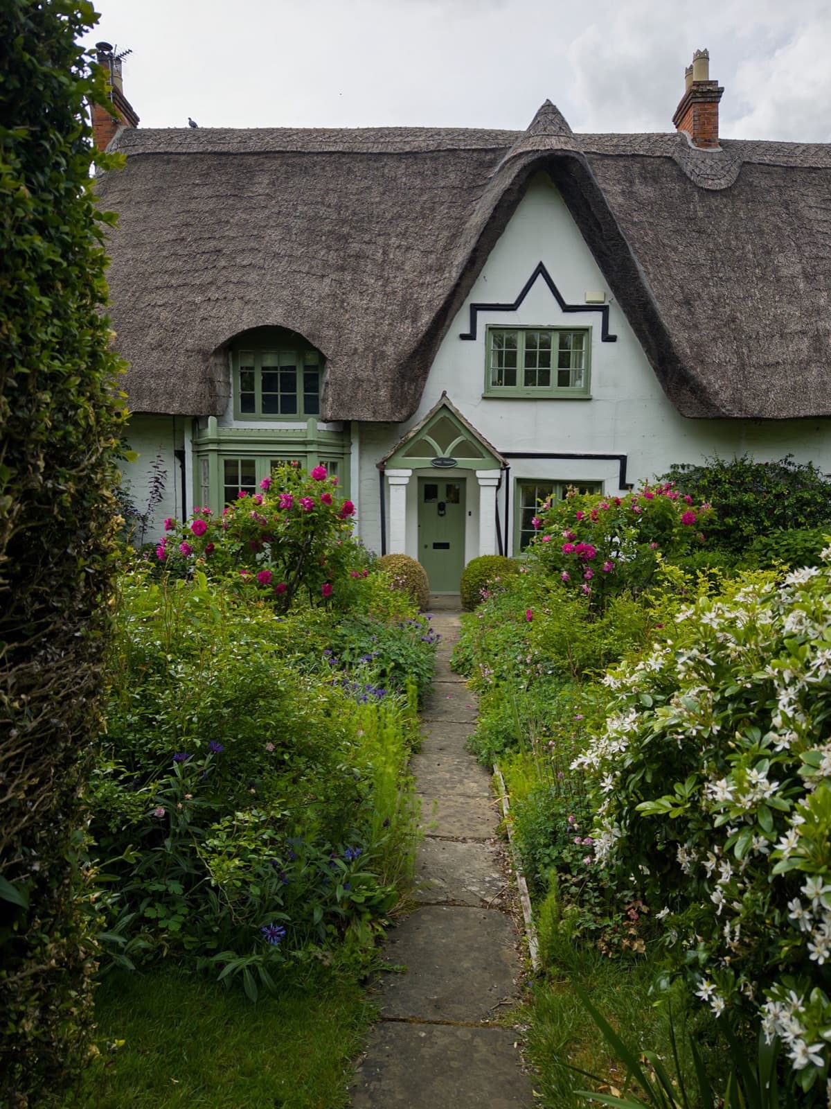 White cottage with a thatched roof surrounded by garden flowers