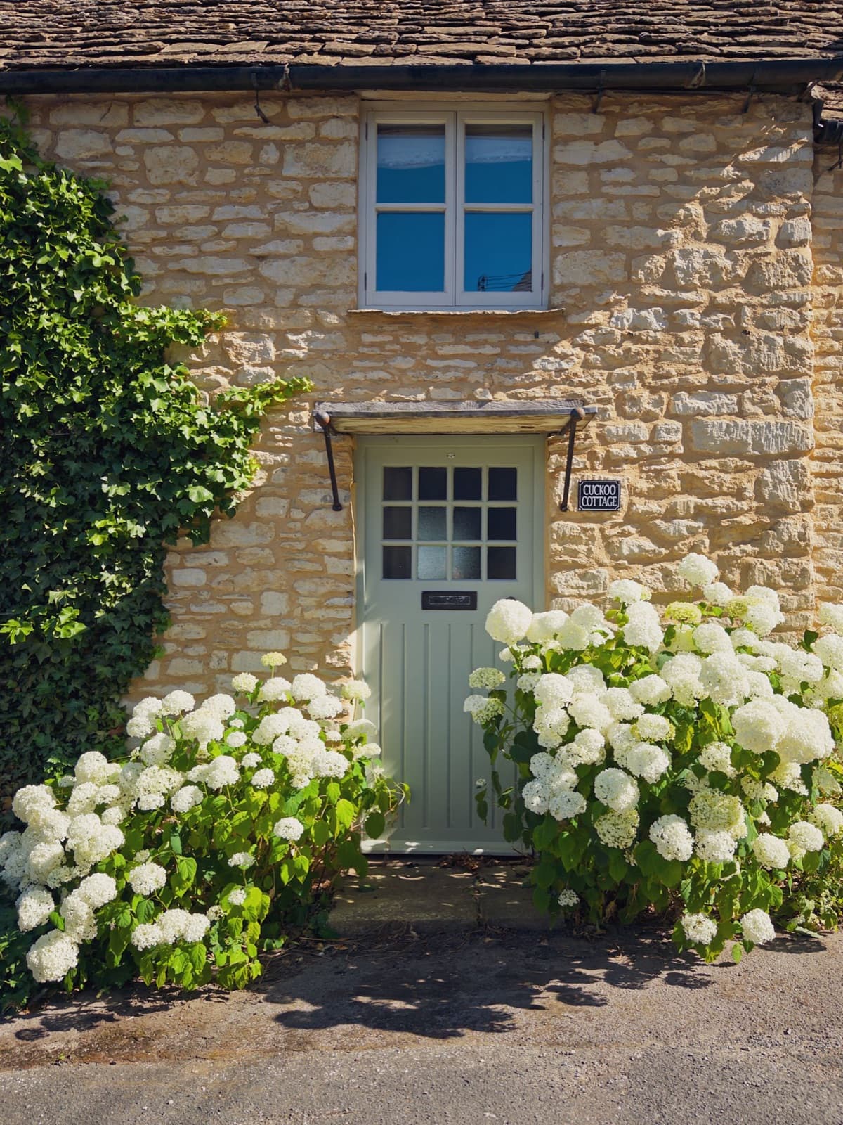 Stone cottage with white hydrangeas under a sunny sky