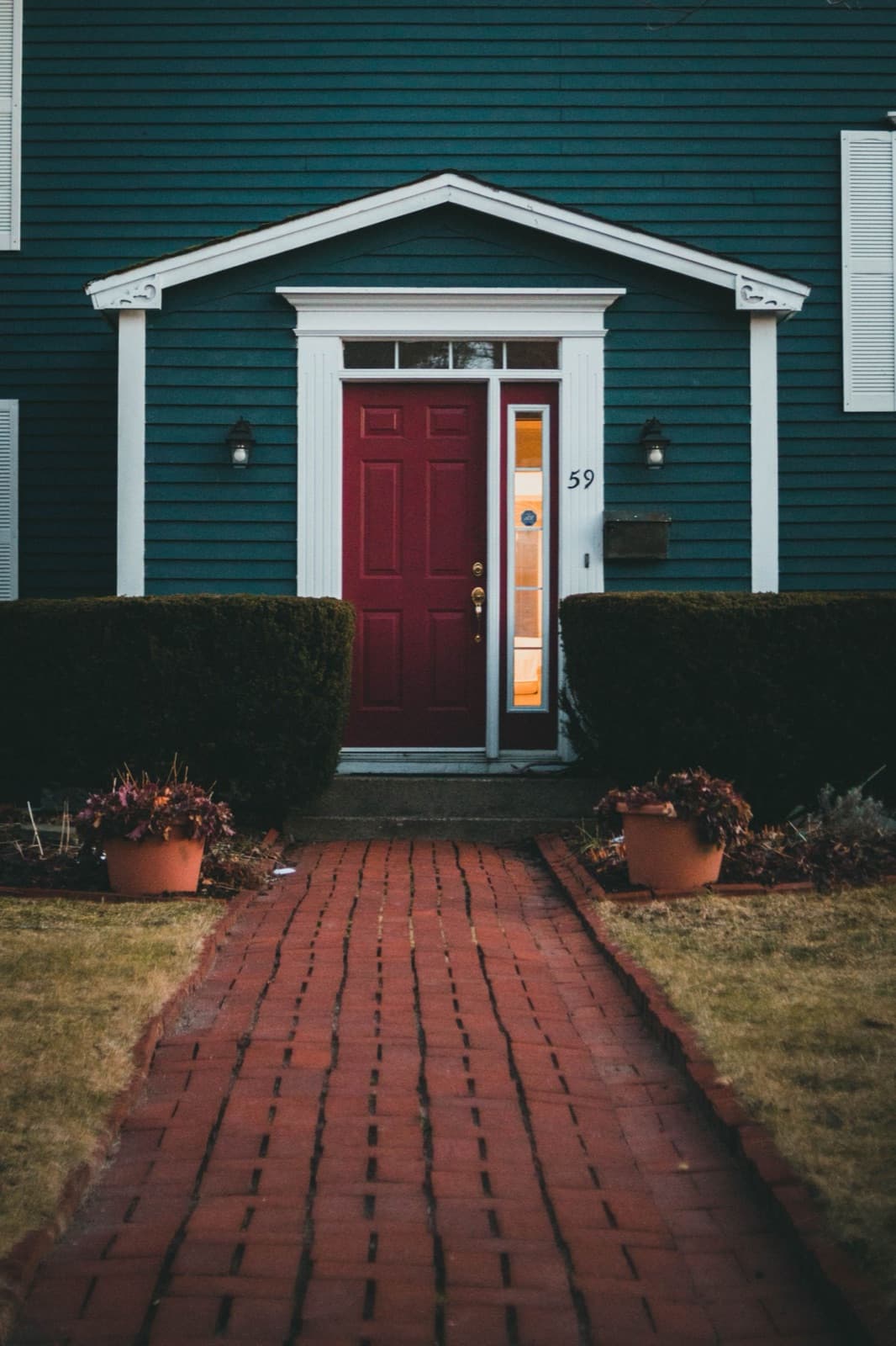 Red door entrance with a brick walkway and bushes