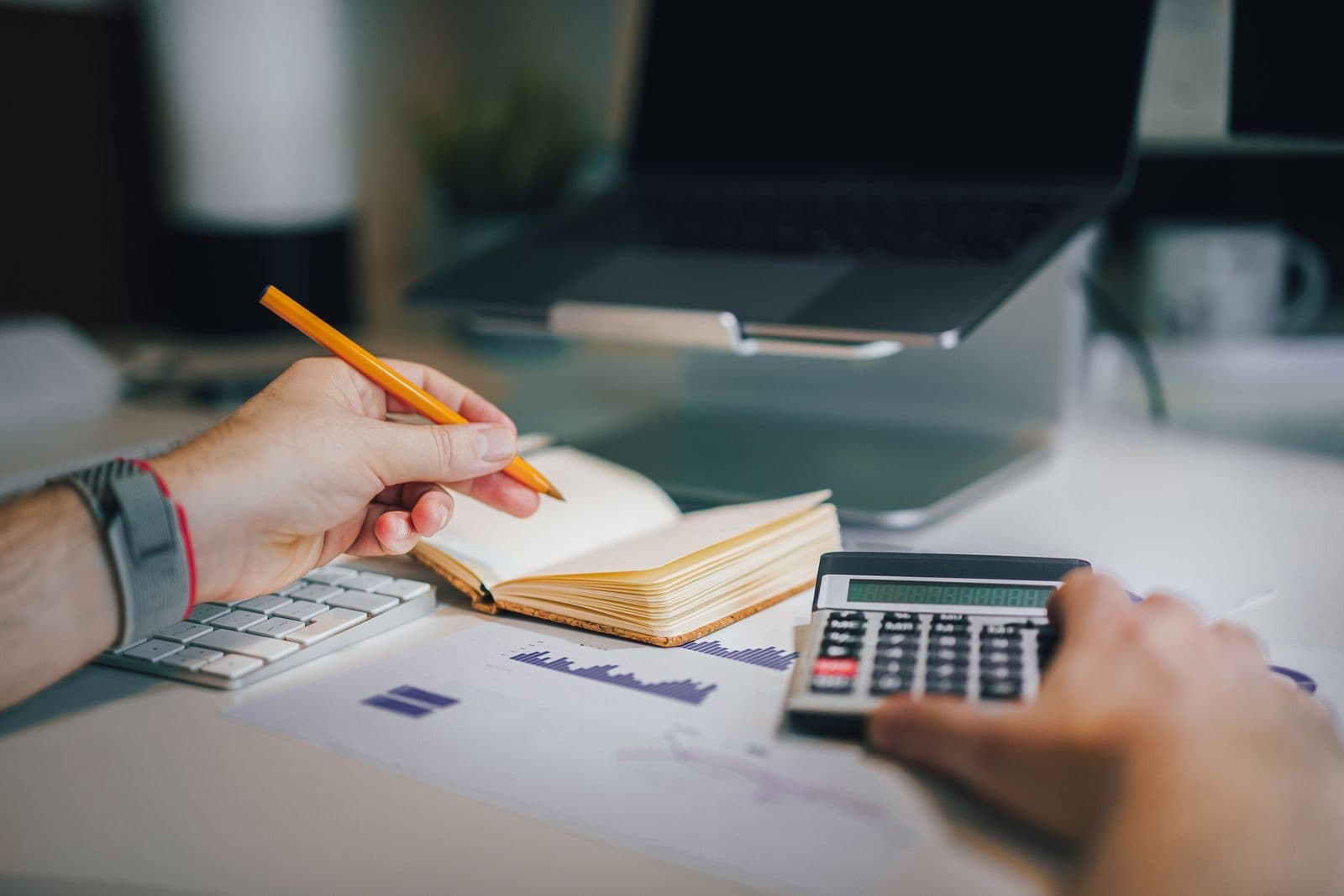 Hands using a calculator and taking notes on a desk