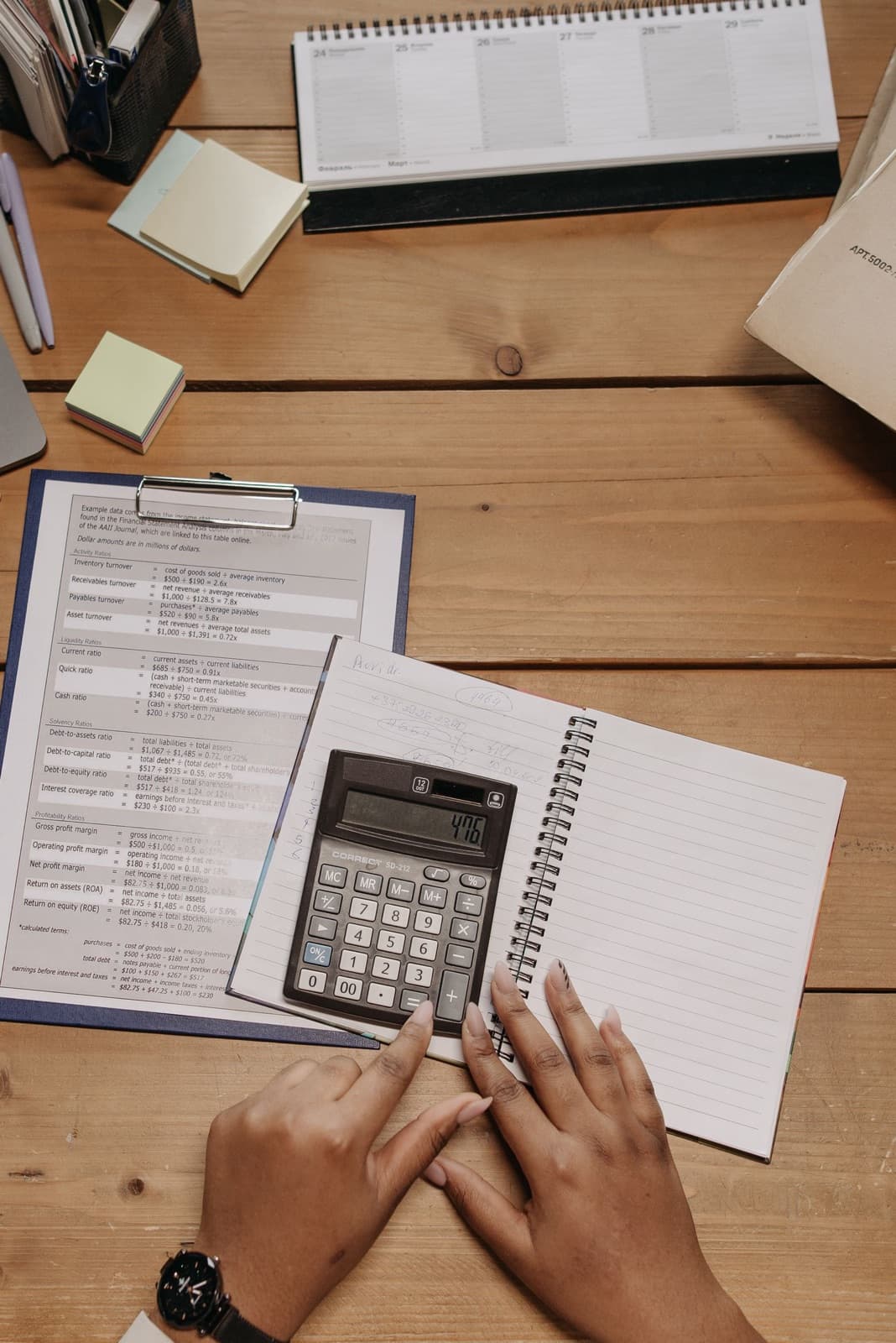 Top view of hands using a calculator on a desk with documents