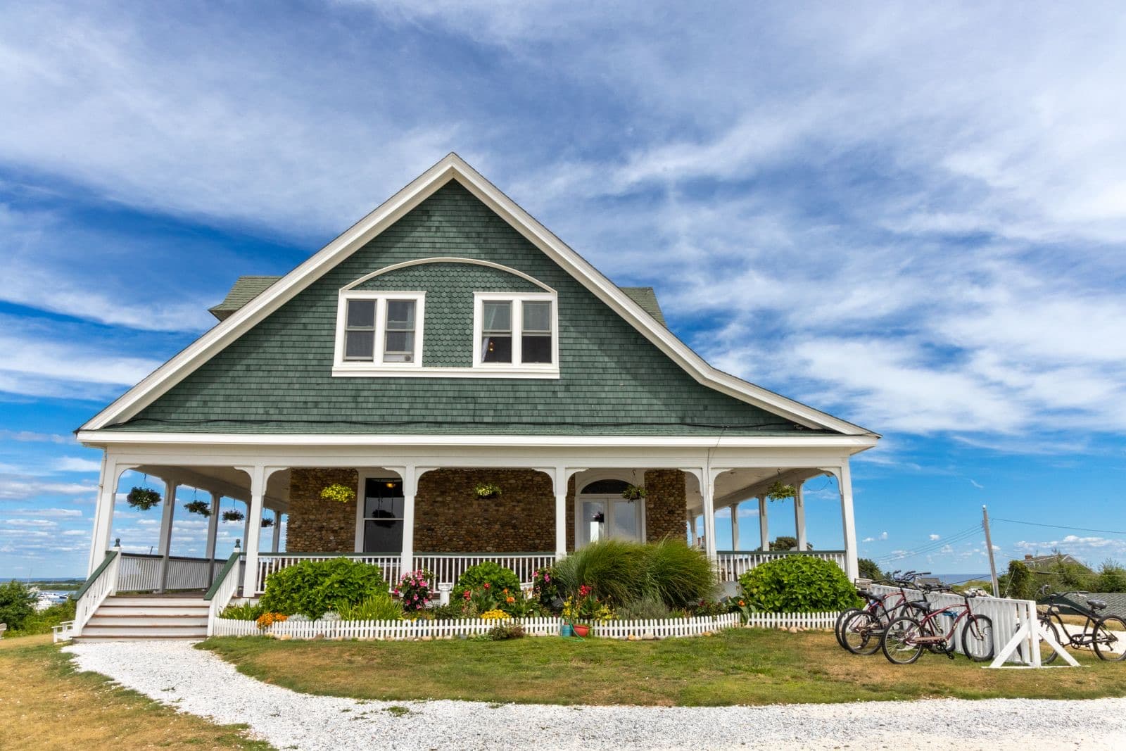 Green-shingled house with a wraparound porch, bicycles out front, and a water view