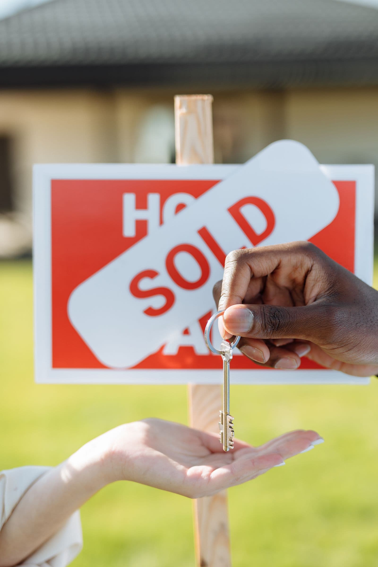 Two hands exchanging a house key in front of a SOLD sign