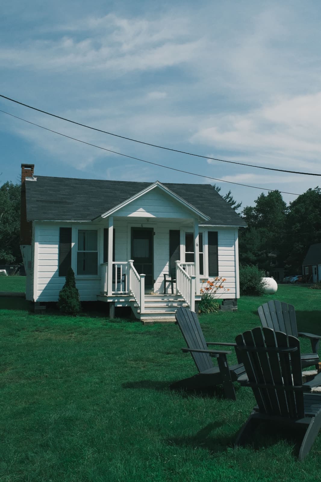 Small white shingled cottage with a covered porch and two Adirondack chairs