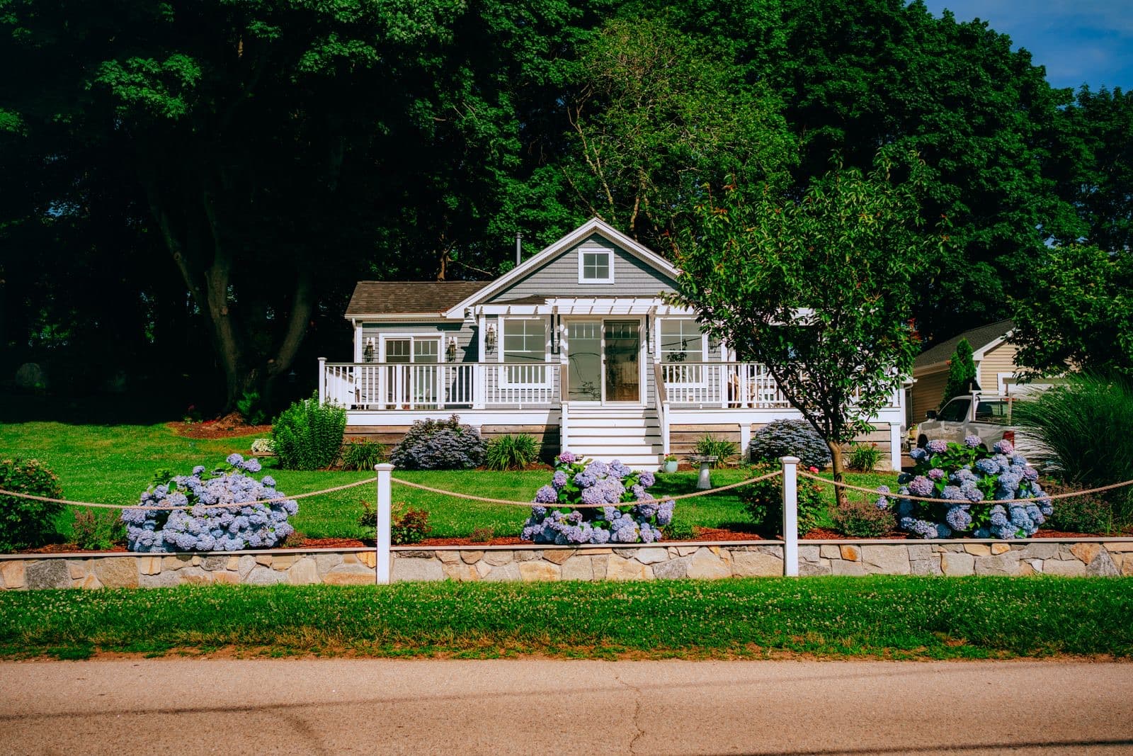 White-shingled cottage with a wraparound porch and blooming hydrangeas